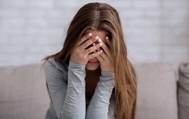 Millennial woman covering her face with hands and crying, feeling depressed or stressed