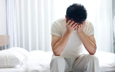 asian man suffering from insomnia sitting on bed head down covering face with hands.