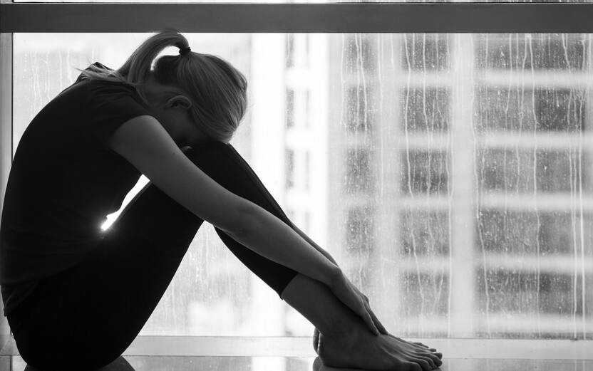 Sadness and despair - Depressed young woman sitting alone at home by the window with city view. Black and white.