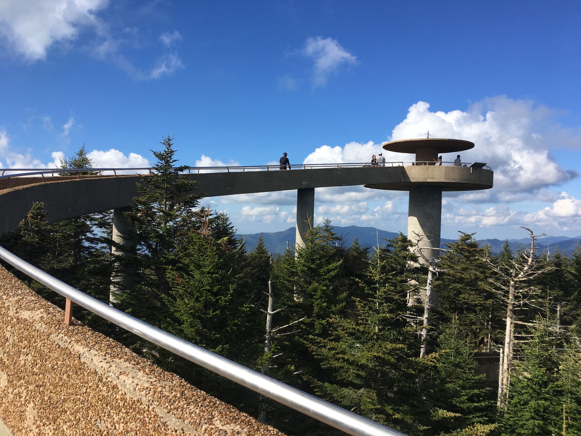 A stone walkway and observation deck fishing above a forest on a sunny day.