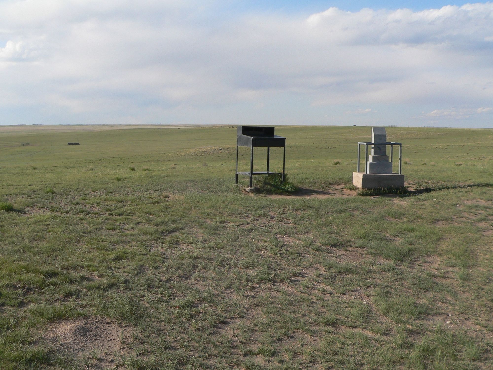 A view of a black registry and a white stone marks in a low-lying expanse of grass.