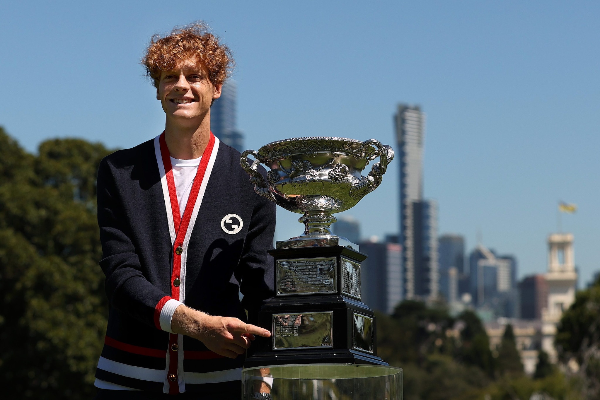 Jannik Sinner con la coppa dell'Australian Open: alle sue spalle la skyline di Melbourne