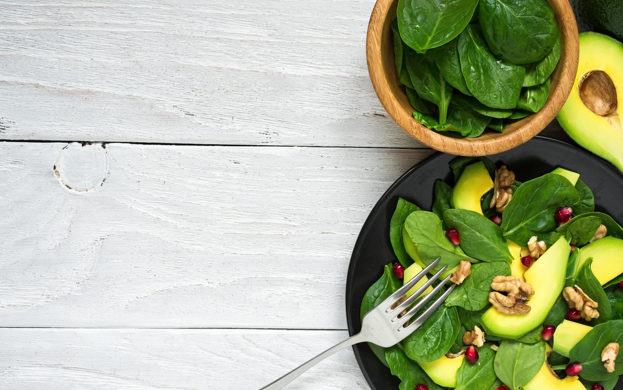 fresh salad with avocado, spinach, pomegranate and walnuts in black plate with fork. healthy food. top view with copy space