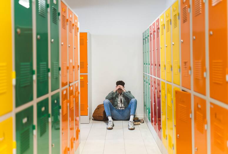 Sad pensive teenager sitting alone in the floor in locker room.