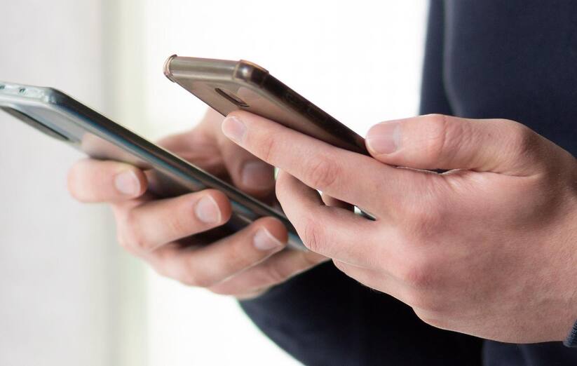 Close up of a man holding two smartphones. Man using two phones at the same time. Busy man standing next to windows and using two smartphones.