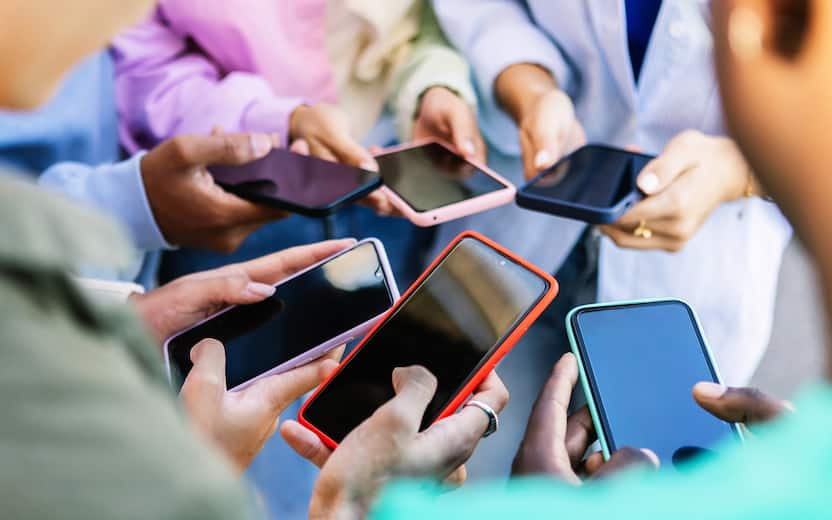 Young group of people standing in circle using mobile phones outside. Unrecognizable teen friends watching social media content on smartphone app. Technology lifestyle concept.