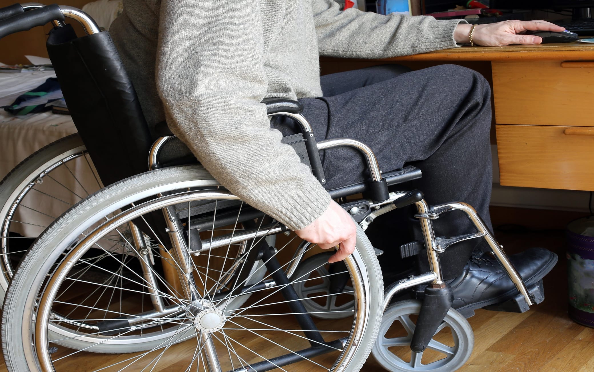 person sitting in a wheelchair at a desk with mouse and pc