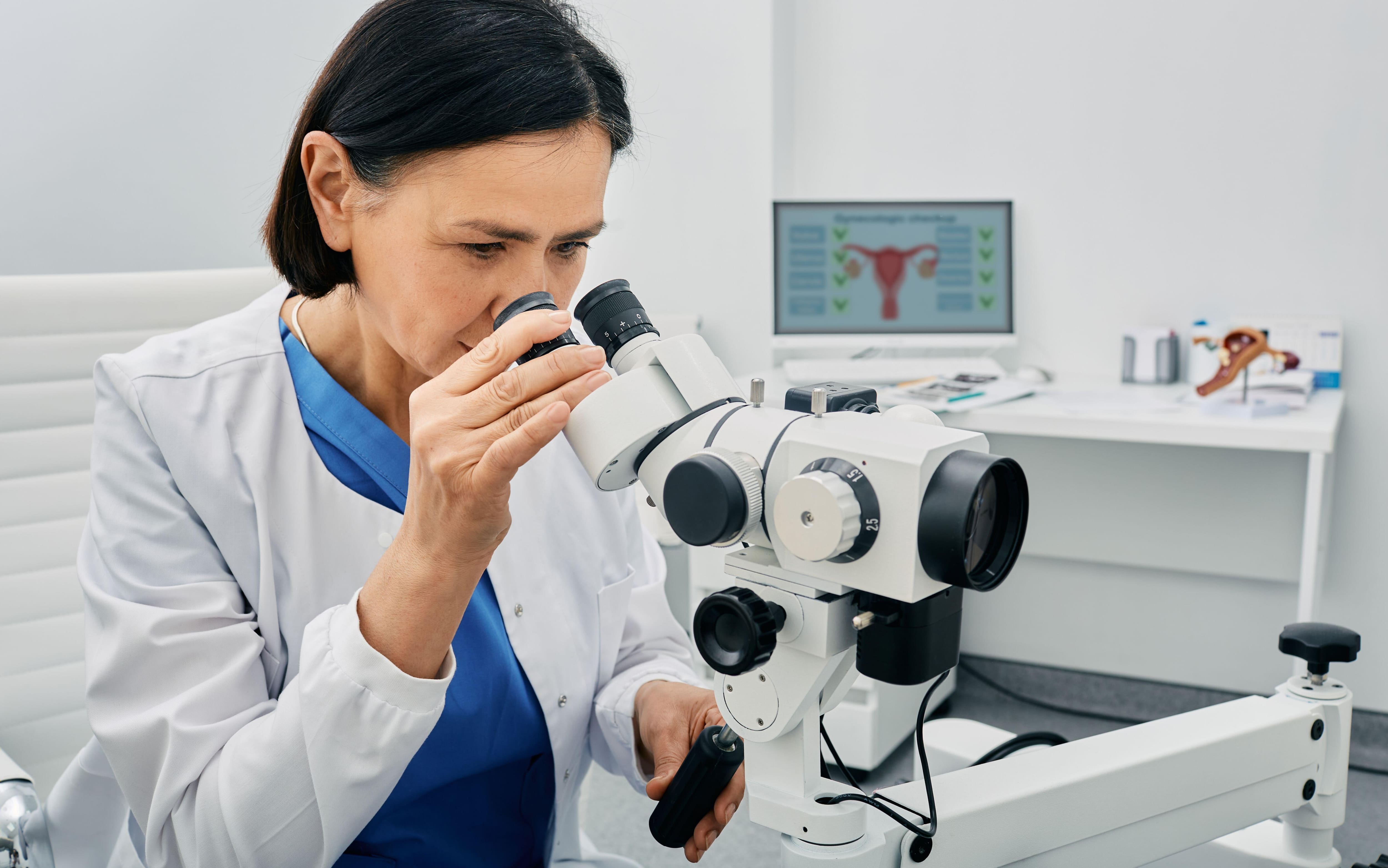 Experienced gynecologist woman sitting near colposcopy in her gynecological office. Profession of gynecologist for women's health