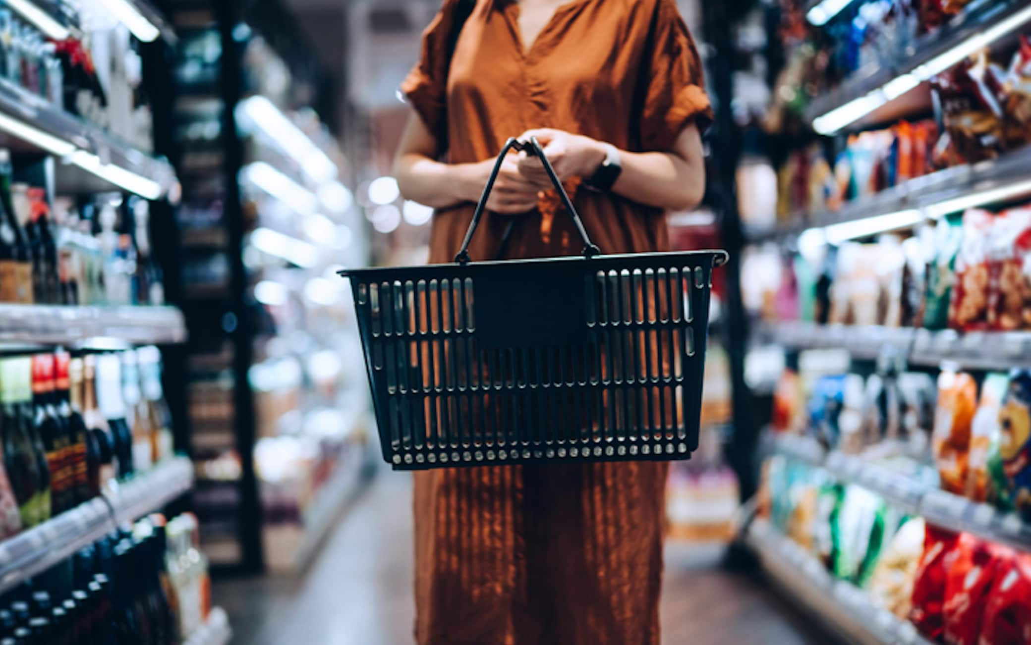 Cropped shot of young woman carrying a shopping basket, standing along the product aisle, grocery shopping for daily necessities in supermarket