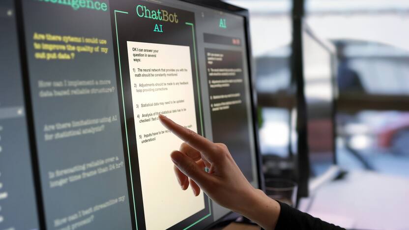 Close-up stock photograph showing a touchscreen monitor being used in an open plan office. A womanâ s hand is asking an AI chatbot pre-typed questions & the Artificial Intelligence website is answering.