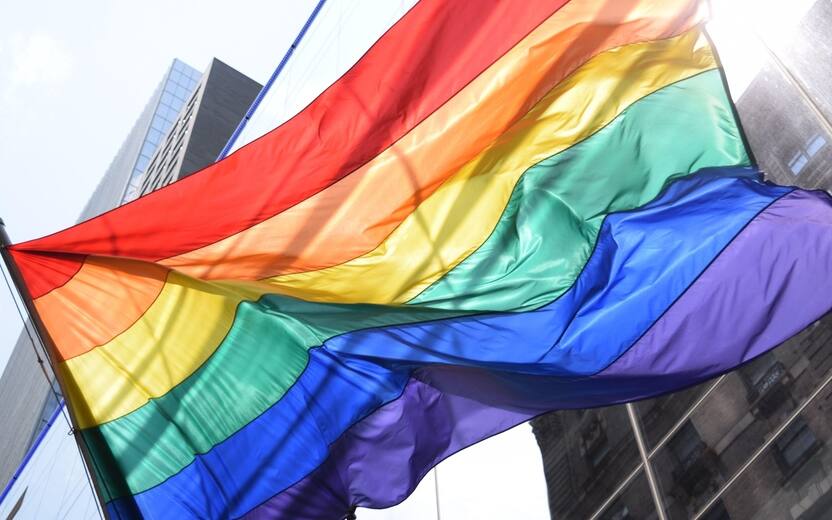 Rainbow flag waving in front of a corporate building in a big city. LGBTQ parade. Equality and love for all.